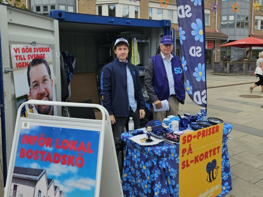 SD-valstuga på Vallentuna torg med två partiföreträdare och profilmaterial.